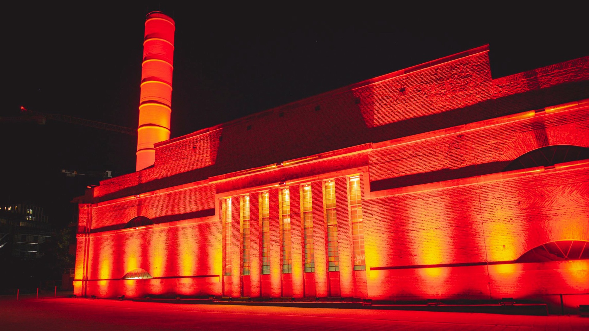 Backsteingebäude mit Schornstein, nachts rot und orange angestrahlt