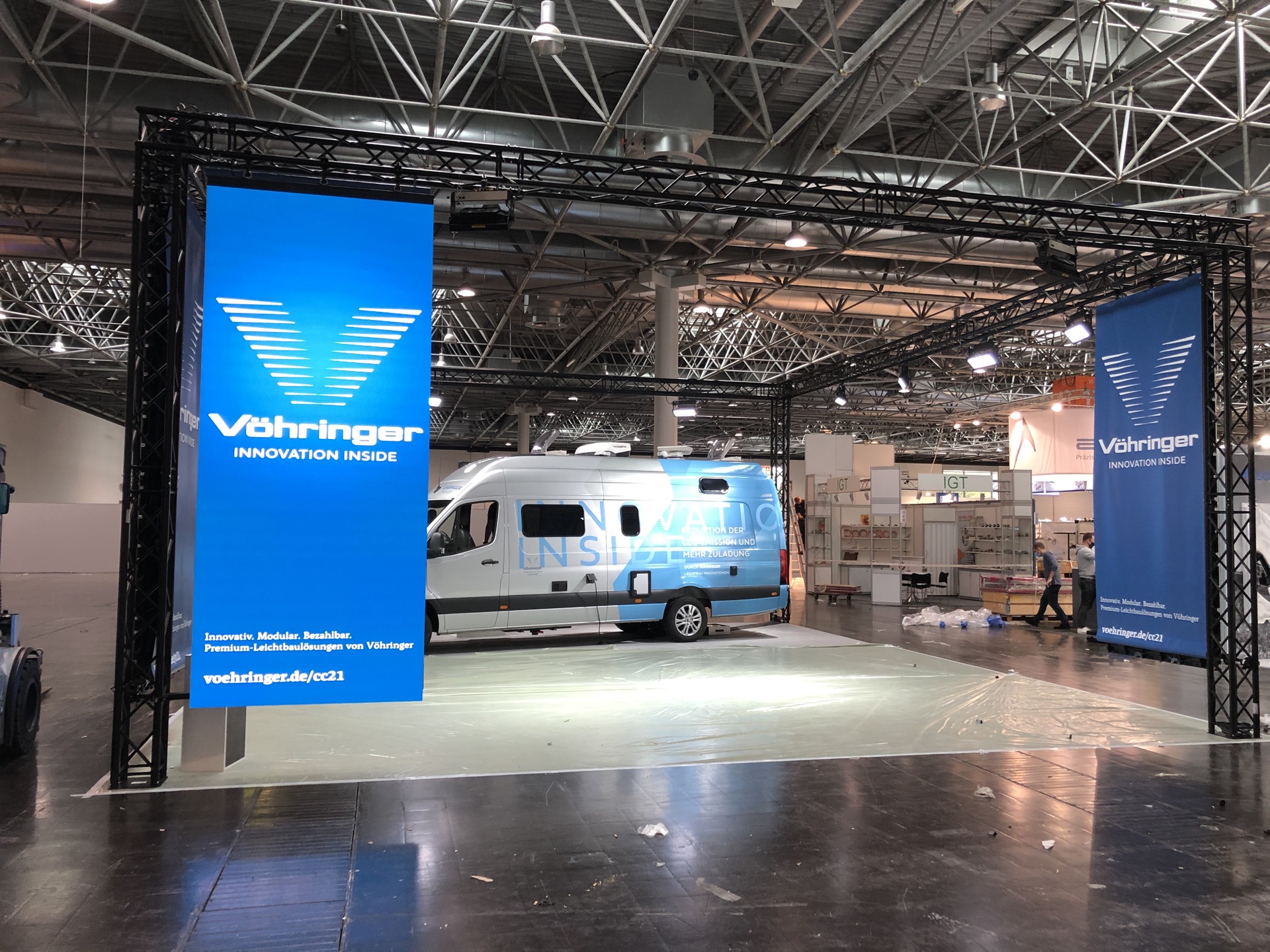 Messestand im Aufbau mit Traversenportal, Bannern und Transporter in einer Messehalle