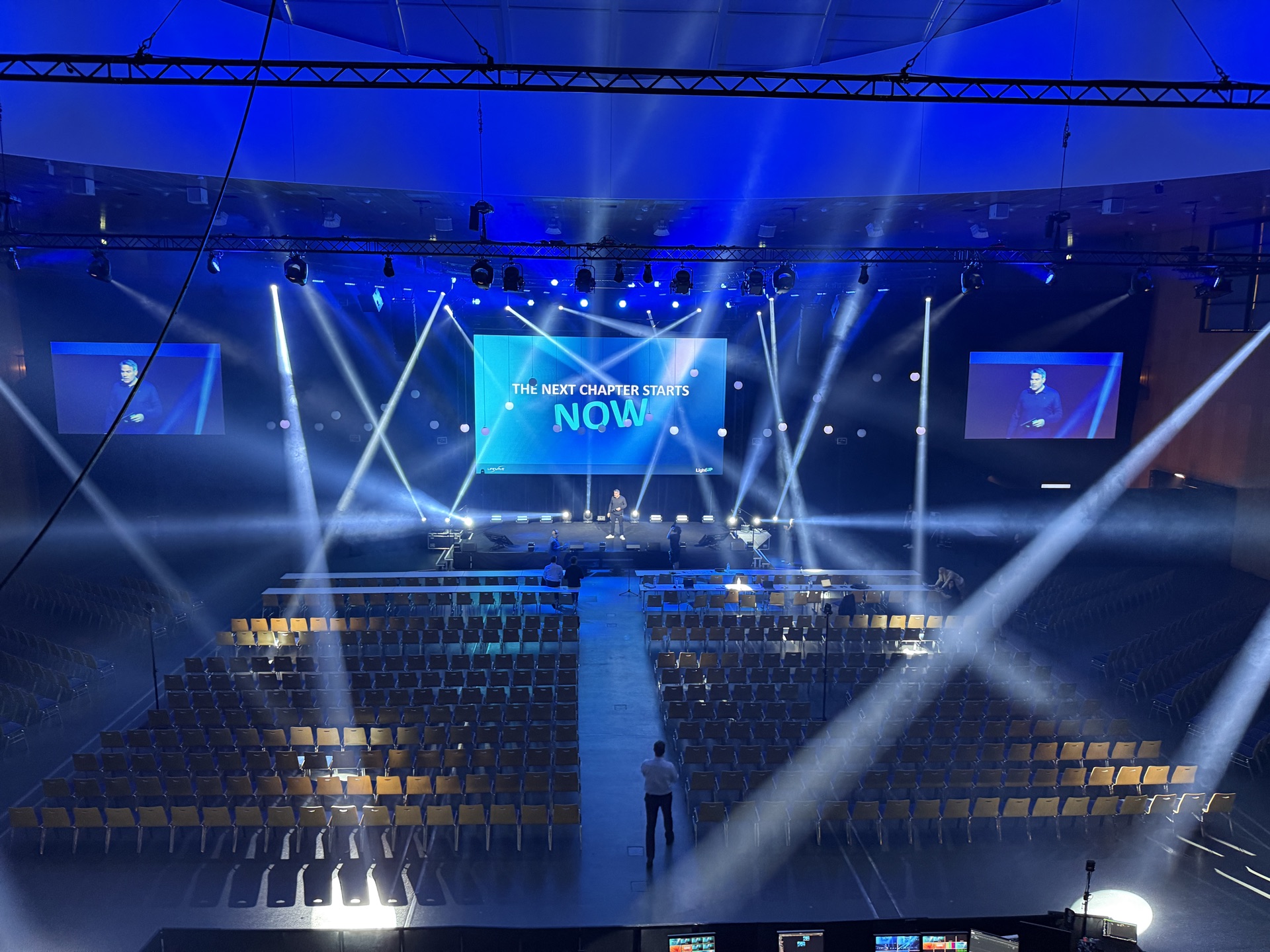 Kongresssaal mit beleuchteter Bühne, großer Bildfläche und Lichtstrahlen im Dunst
