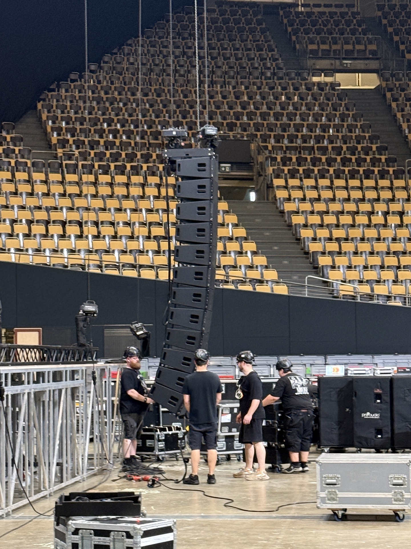 Vier Techniker hängen ein Line-Array in einer leeren Arena