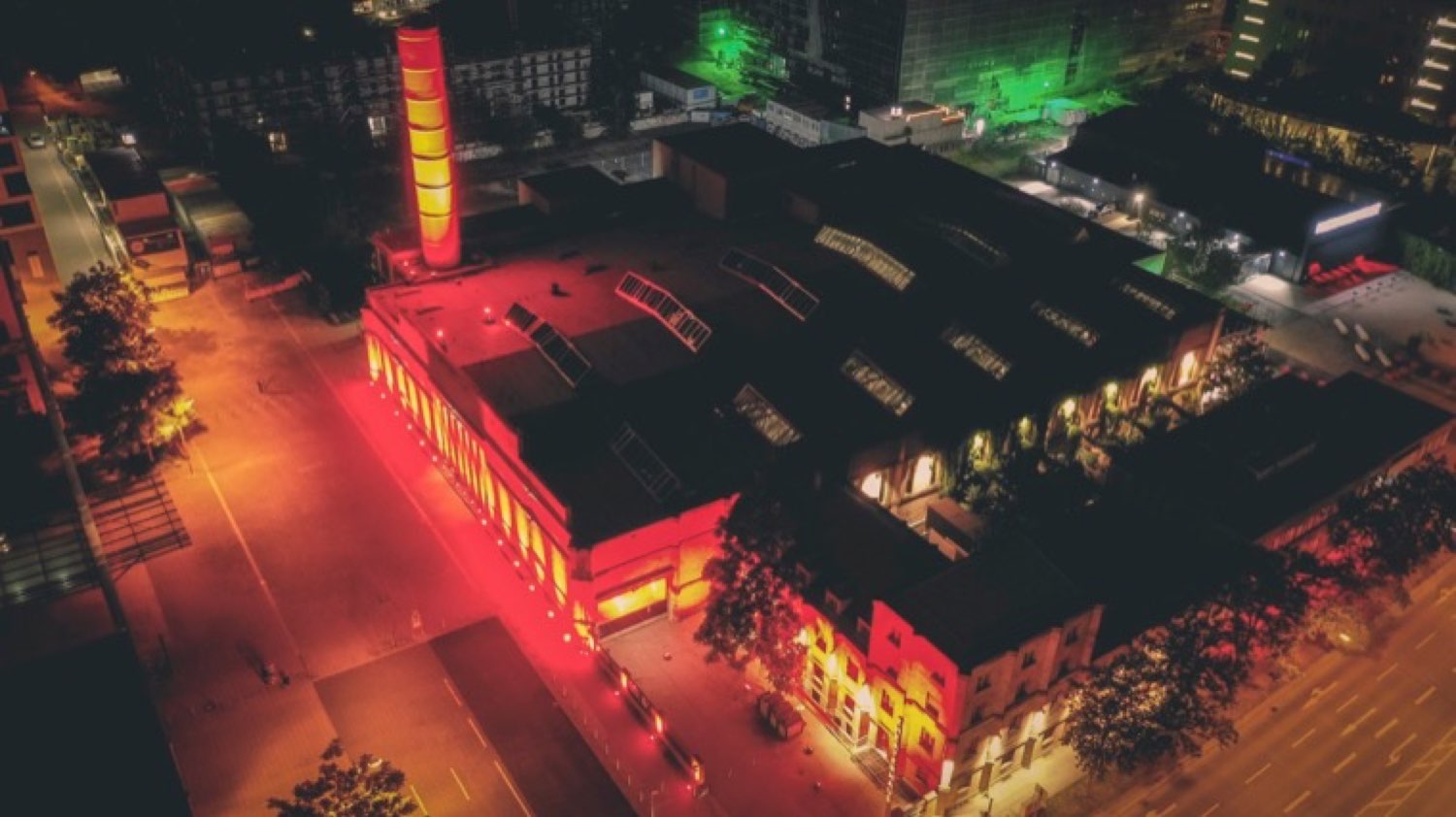 Industriegebäude bei Nacht in Rot und Gelb illuminiert, Luftaufnahme