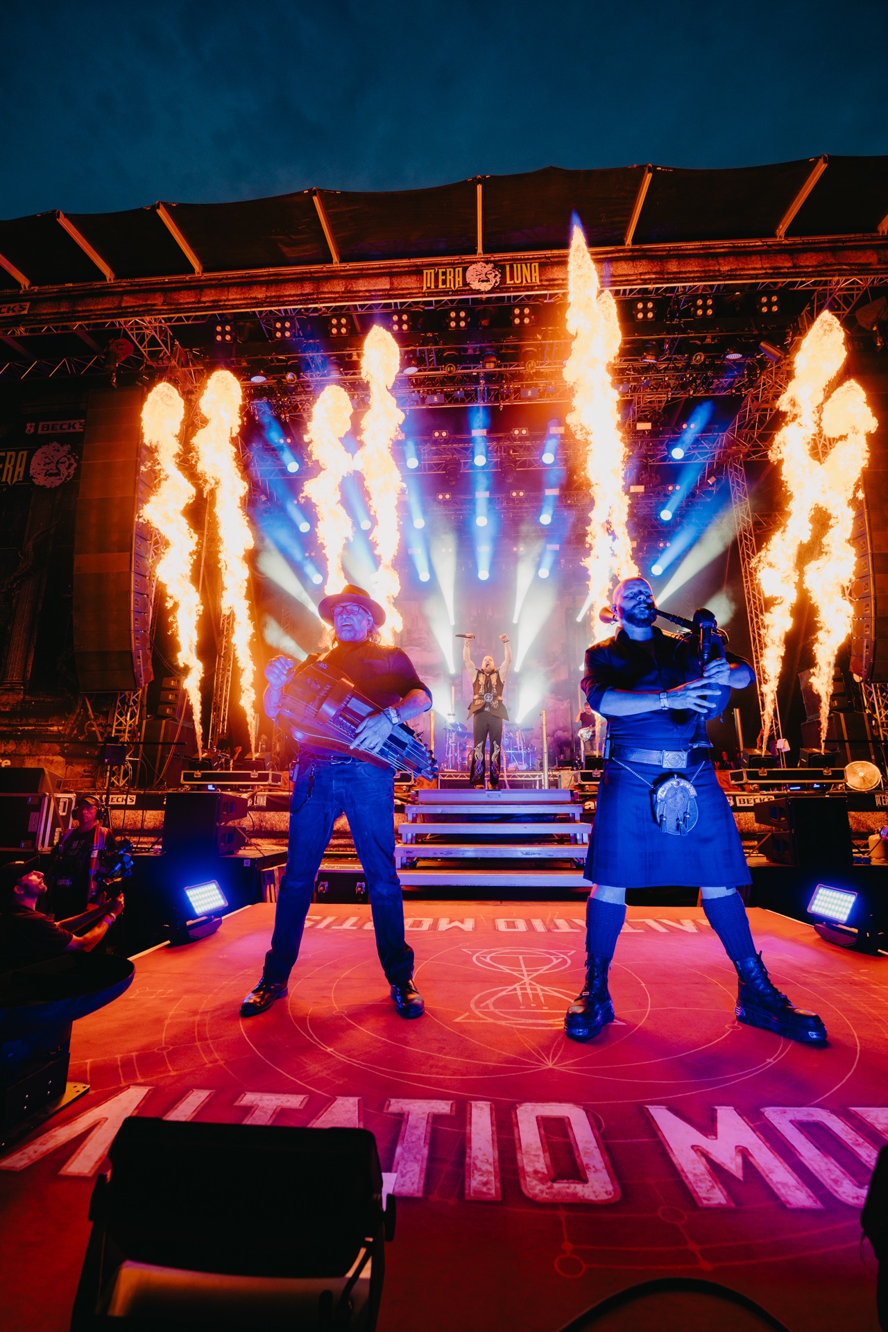 Zwei Musiker auf der Bühne vor Flammensäulen und blauen Lichtstrahlen