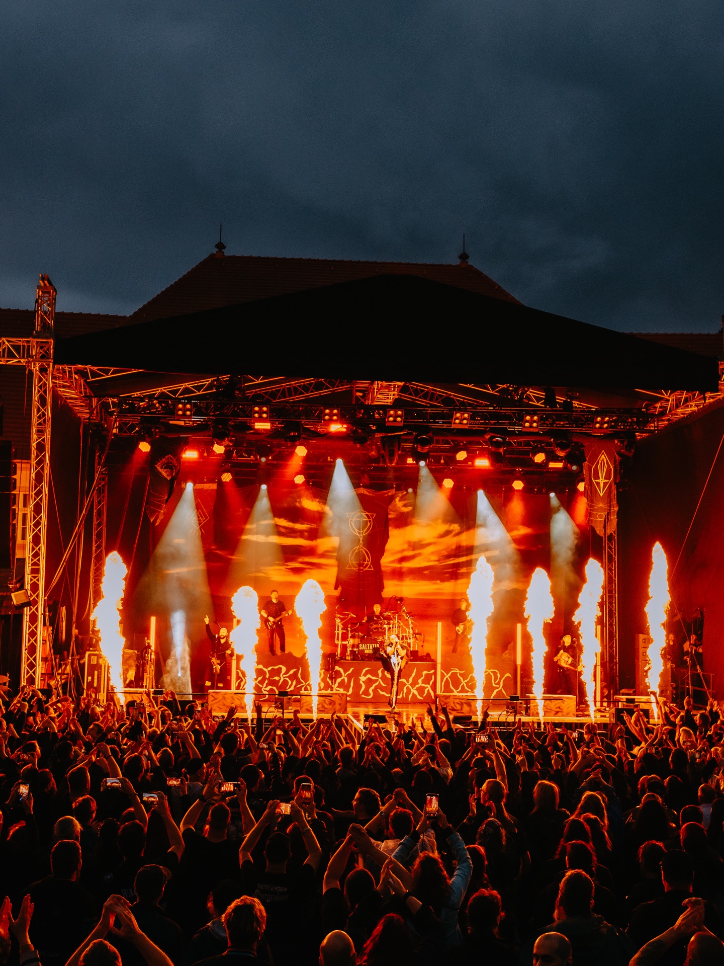 Open-Air-Bühne vor einem Schloss mit Flammensäulen und Publikum bei Dämmerung