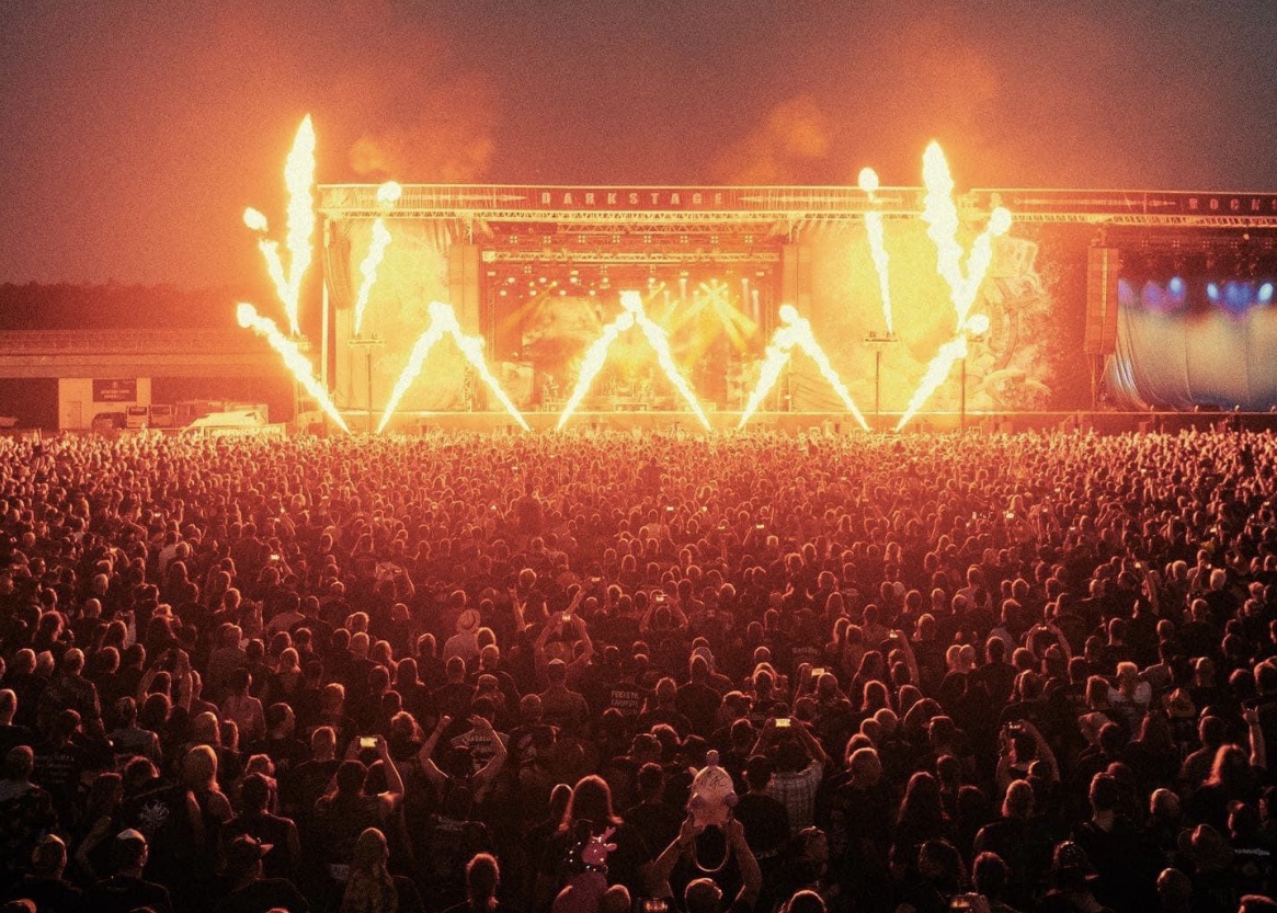 Festivalpublikum vor einer Open-Air-Bühne mit hohen Flammensäulen