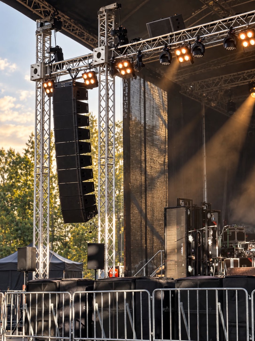 Line-Array und Scheinwerfer an den Traversen einer Open-Air-Bühne im Abendlicht