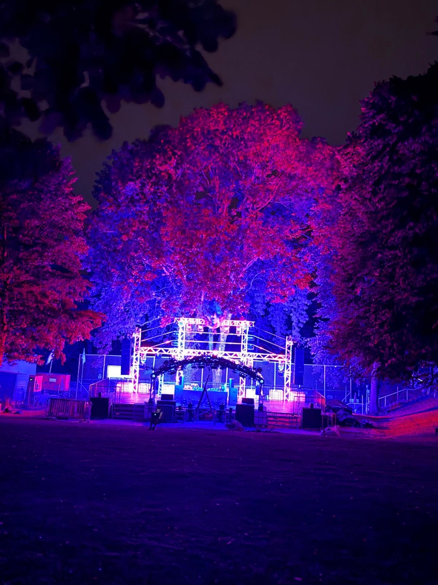 Bühne mit Traversen unter rot und blau angestrahlten Bäumen bei Nacht