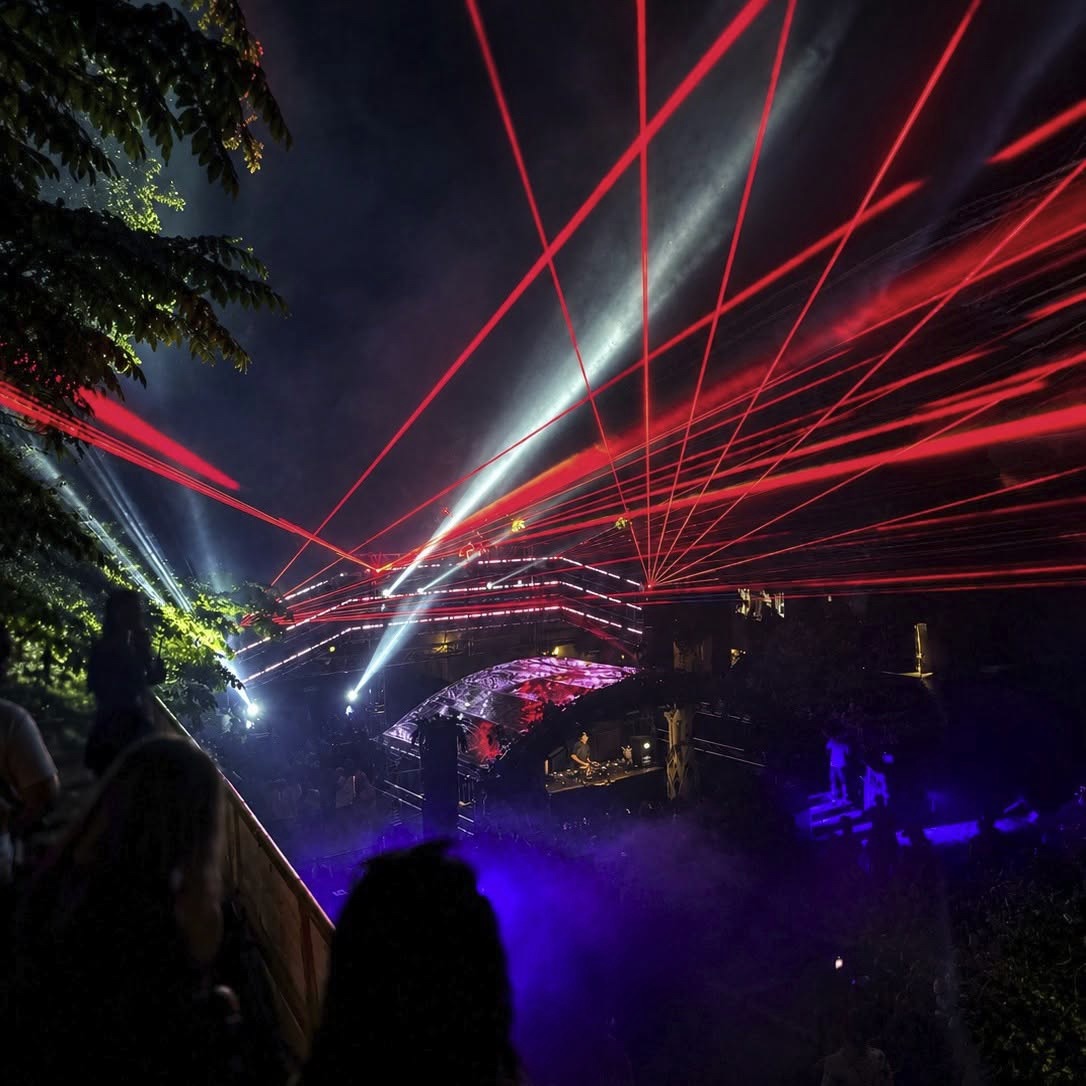 Rote Laserstrahlen über einer Bühne zwischen Bäumen bei Nacht